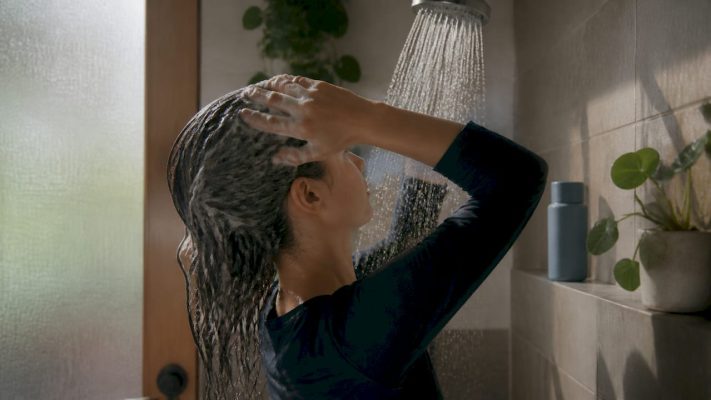 Hands rinsing hair over bathroom sink with aloe plant