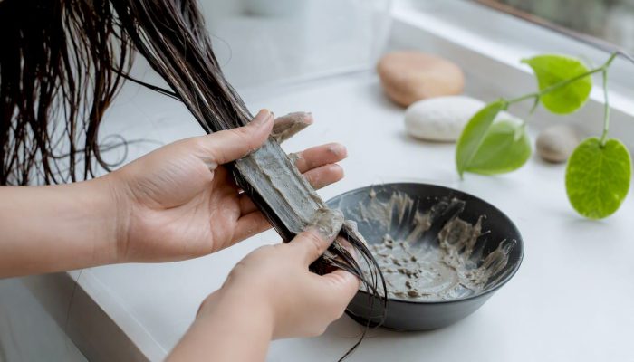 Hands applying bentonite clay to hair strands