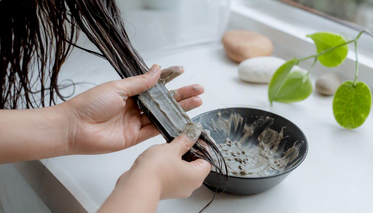 Hands applying bentonite clay to hair strands