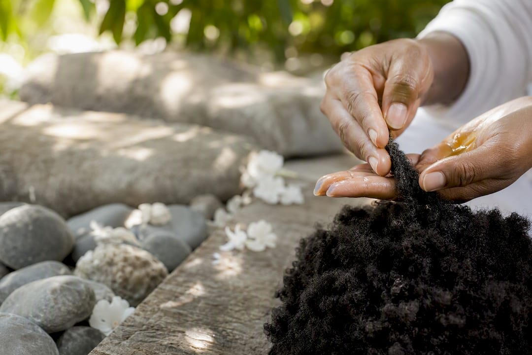 Hands applying cleansing solution to coiled hair with leaves