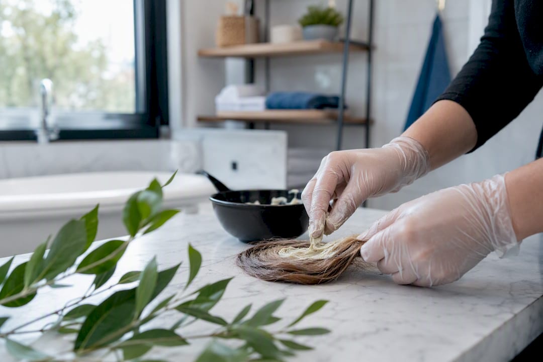 Hands applying bleach to coiled hair on leaf
