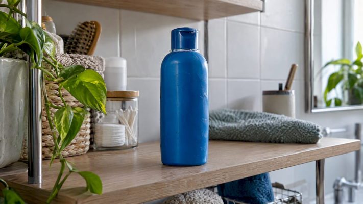 Blue shampoo bottle beside a fresh green leaf