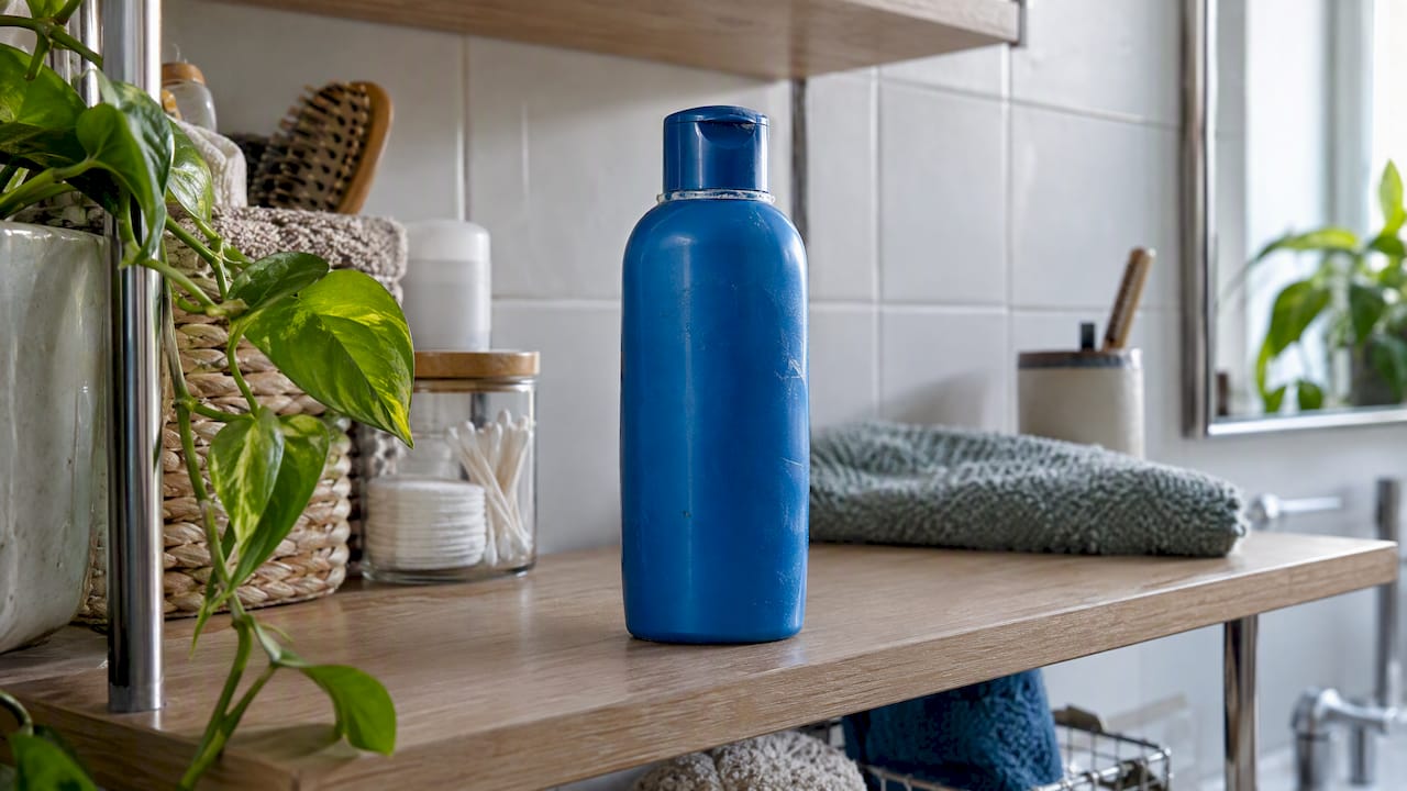 Blue shampoo bottle beside a fresh green leaf